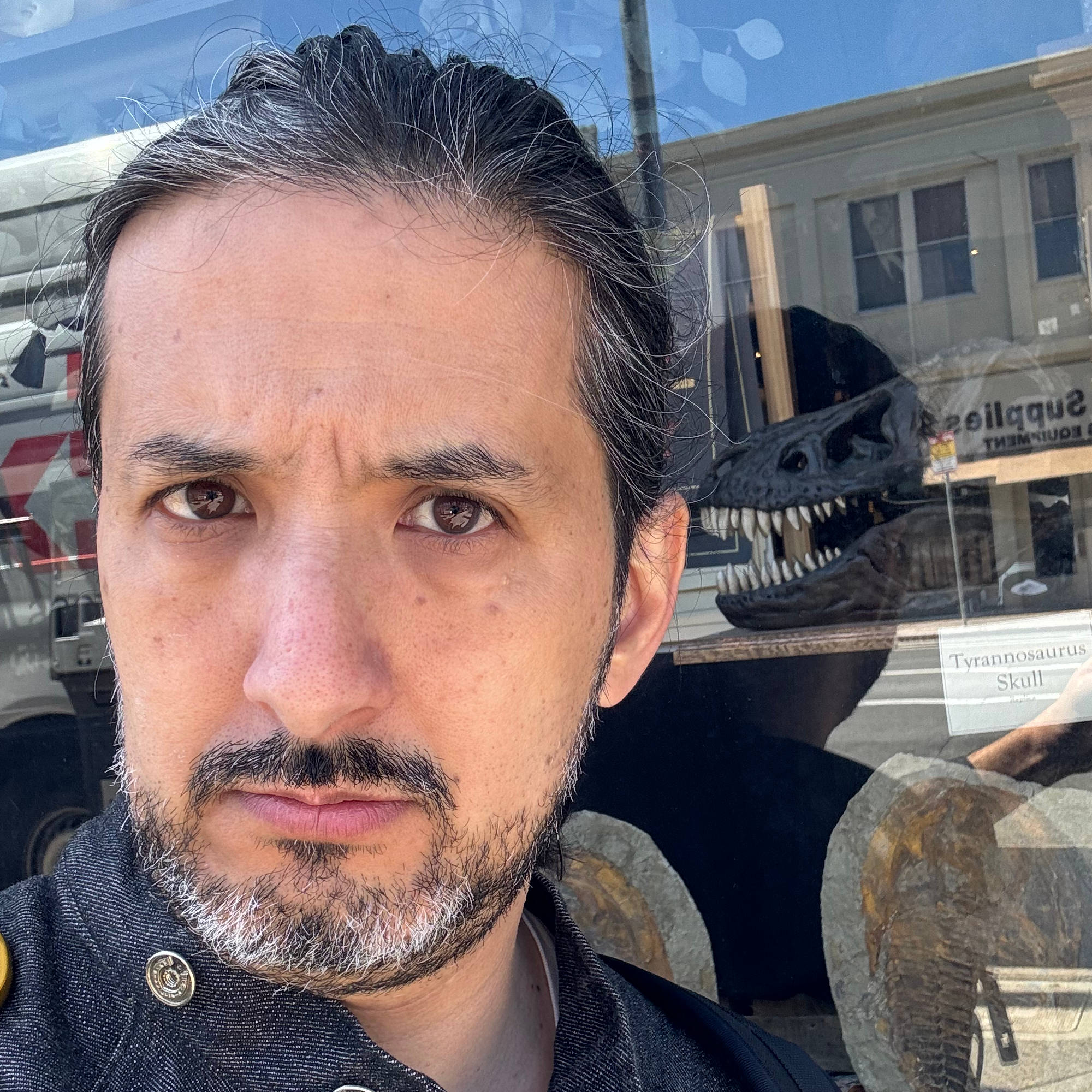 Dan looks inquisitive and slightly serious in front of a dinosaur.